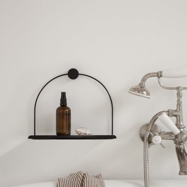 A black metal shelf attached to a bathroom wall, holding a brown glass bottle and a shell