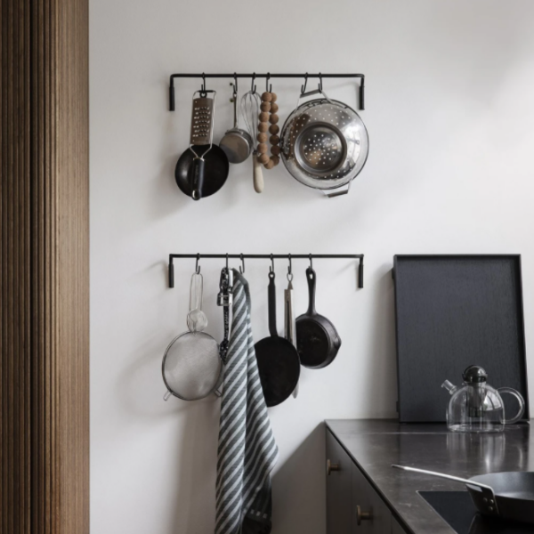 Kitchen setup with black metal rails holding pans, utensils, and a towel