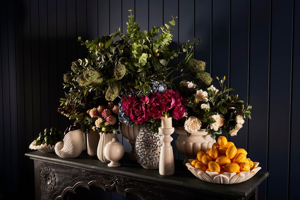 A decorative table display with vibrant flowers, bowls of fruit, and limes