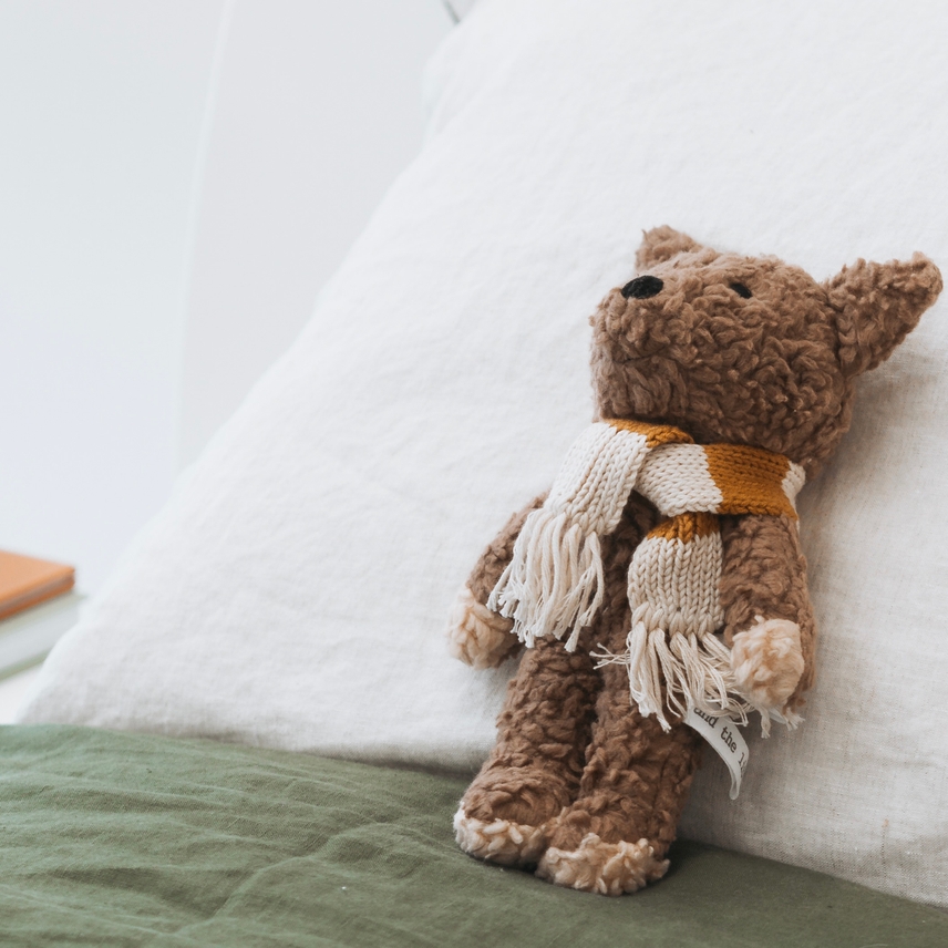 a brown teddy bear sitting on top of a white pillow