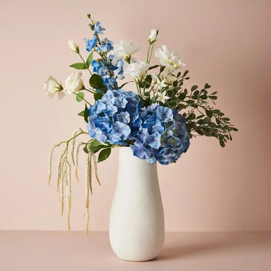 a white vase filled with blue and white flowers