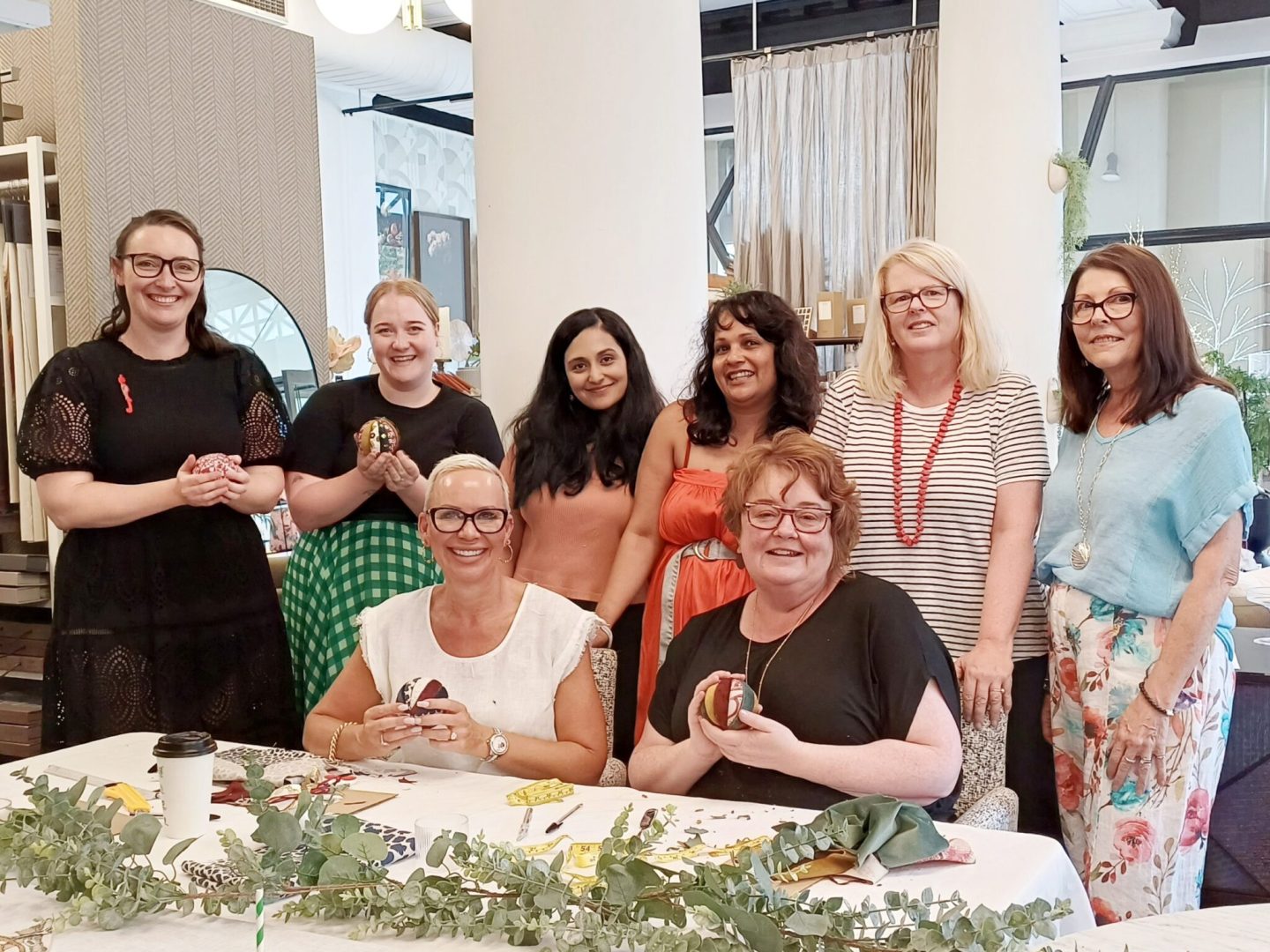 Group of women smiling during a Christmas workshop, holding small crafted items in a design studio.